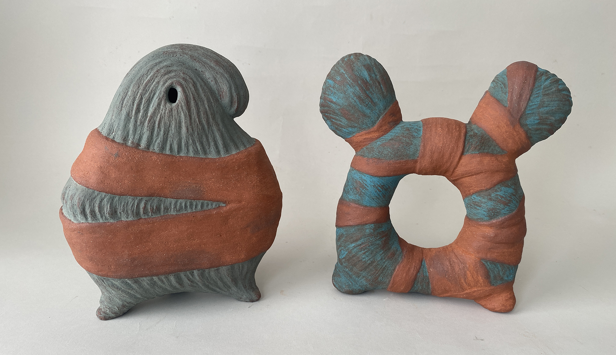 Two ceramic sculptures by Maria Porges, in a green shade with orange bands wrapping around them.